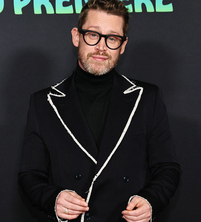 Macaulay Culkin wearing glasses and a black suit with white trim at a premiere event, looking confident and relaxed Macaulay Culkin wearing glasses and a black suit with white trim at a premiere event, looking confident and relaxed