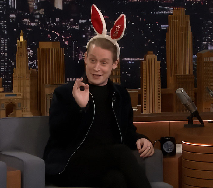 Macaulay Culkin wearing bunny ears on a late night talk show, smiling and gesturing with his hand. Macaulay Culkin wearing bunny ears on a late night talk show, smiling and gesturing with his hand.