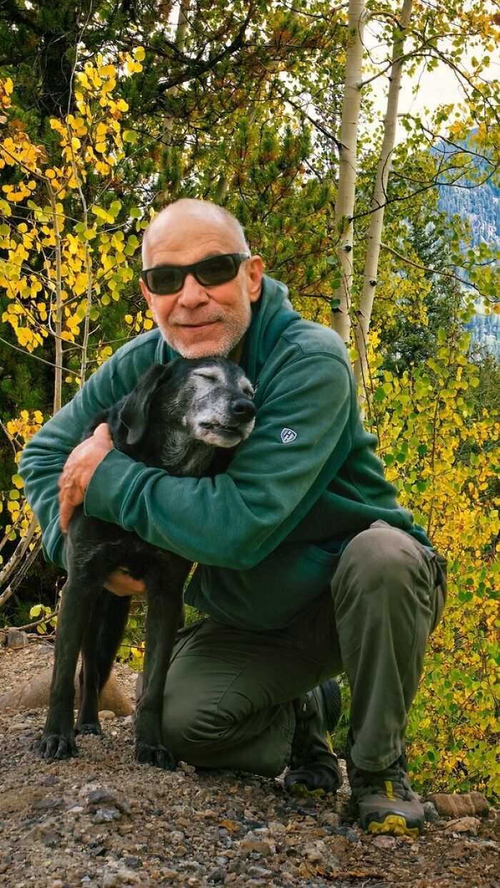 Man in sunglasses hugging dog outdoors surrounded by autumn trees, reflecting on people who regret having kids.