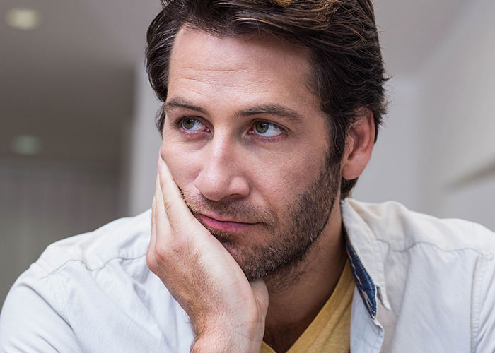 Man with a thoughtful expression resting his face on his hand, reflecting on teen’s rude attitude and family struggles.