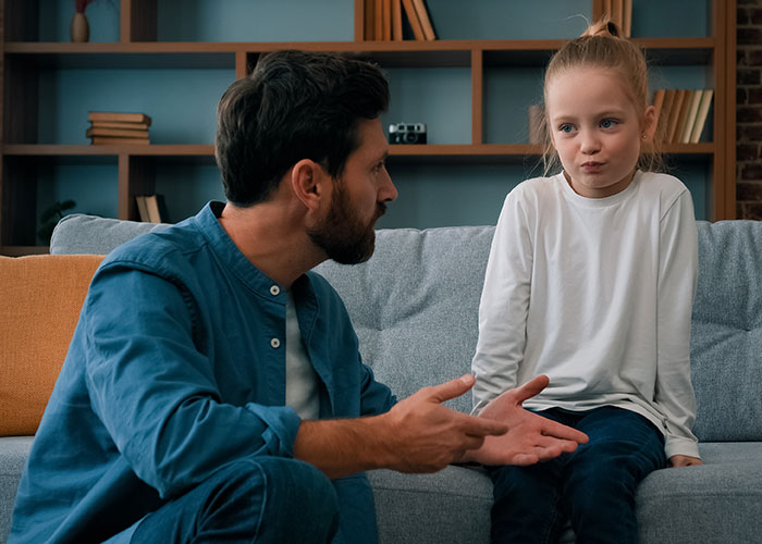 Man sitting on couch talking to a young girl showing rude attitude, illustrating family tension and conflict.