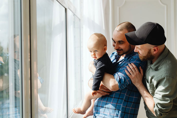 Man holding baby near window with another man standing close by, depicting family surprise on Christmas visit. Man holding baby near window with another man standing close by, depicting family surprise on Christmas visit.