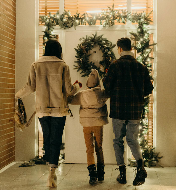 Family arriving at decorated front door with Christmas wreath, attempting surprise visit late at night during holiday season.