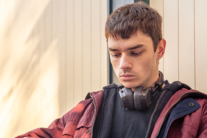 Young man looking down with headphones around his neck, illustrating a guy annoyed at being a free babysitter.
