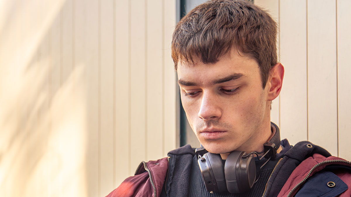 Young man with headphones around his neck looking down, reflecting on responsibility towards girlfriend's son.