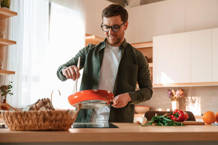 Man cooking in kitchen preparing food, representing trad wife controversy over man doing womanly things.