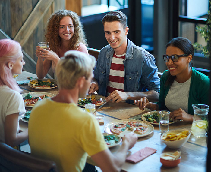 Group of friends enjoying pizza and salad at a dining table, illustrating tension around rich man refusing to pay for cake ordered.