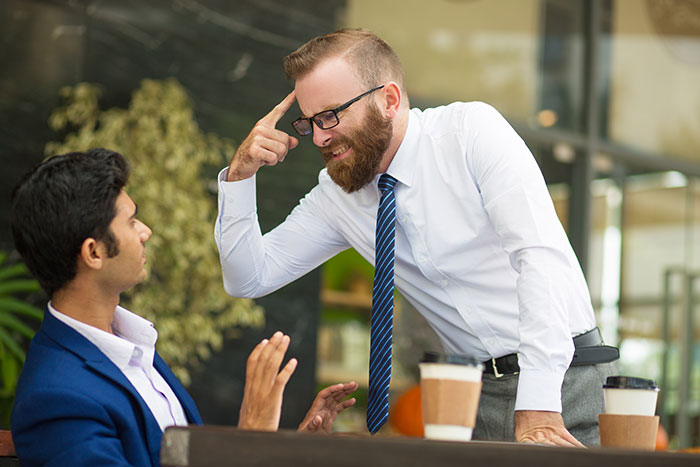 Manager expressing frustration to employee taking time off during a tense office conversation with coffee cups on the table. Manager expressing frustration to employee taking time off during a tense office conversation with coffee cups on the table.