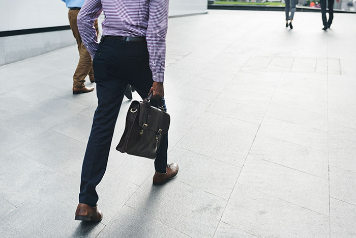 Employee walking away from office building holding briefcase, illustrating manager letting employee take time off. Employee walking away from office building holding briefcase, illustrating manager letting employee take time off.
