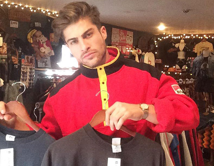 Young man styled like the next Brad Pitt, wearing a red jacket, holding two shirts in a vintage clothing store. Young man styled like the next Brad Pitt, wearing a red jacket, holding two shirts in a vintage clothing store.