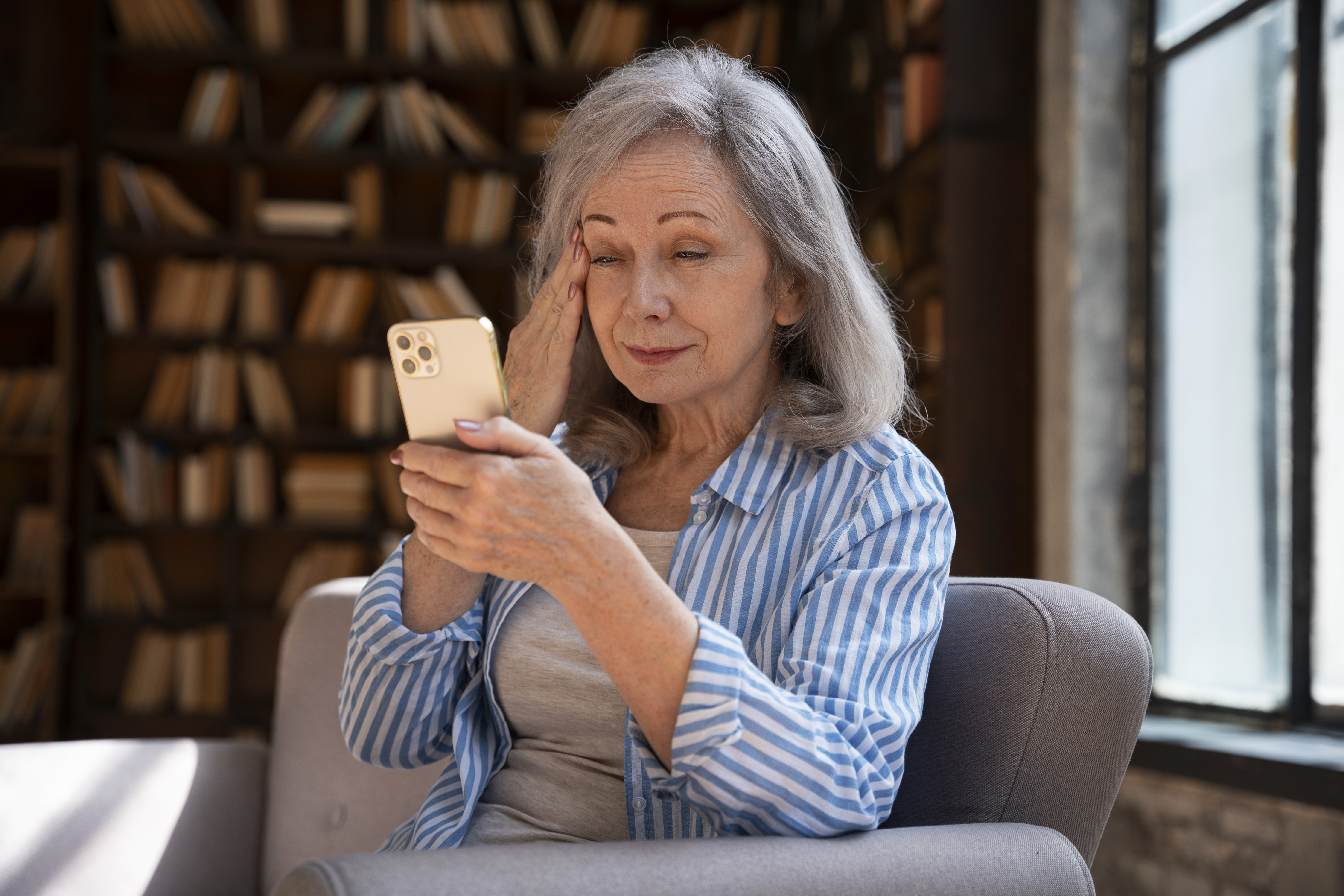 Older woman with gray hair in striped shirt looking surprised while holding a phone at home, related to bride savage revenge MIL.