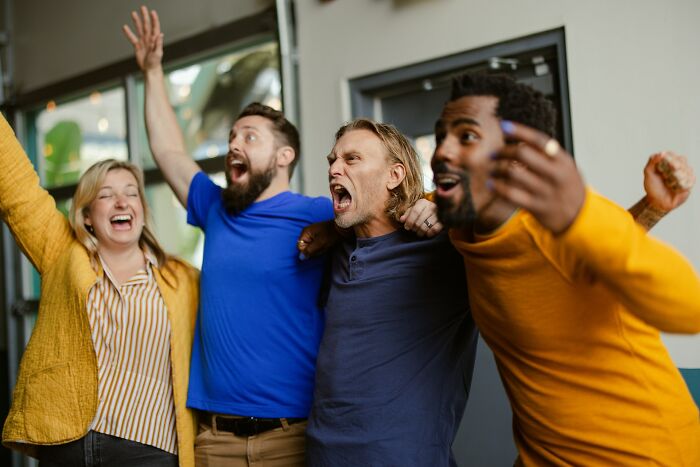 Group of diverse adults cheering excitedly indoors, capturing moments of realizing childhood habits were unusual.