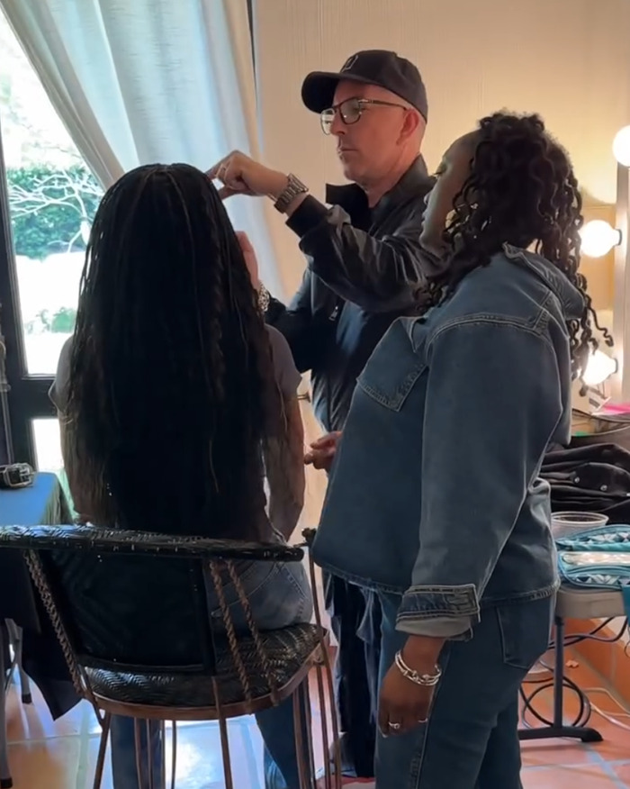 Michelle Obama with ultra-long hair getting her casual look styled by two hairstylists in a bright room.