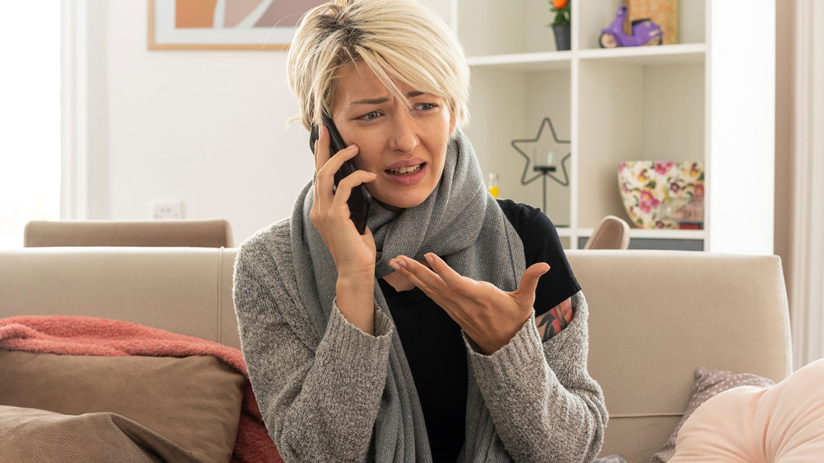 Woman wrapped in scarf looking upset while talking on phone, reflecting family holiday conflict with sick DIL exclusion.