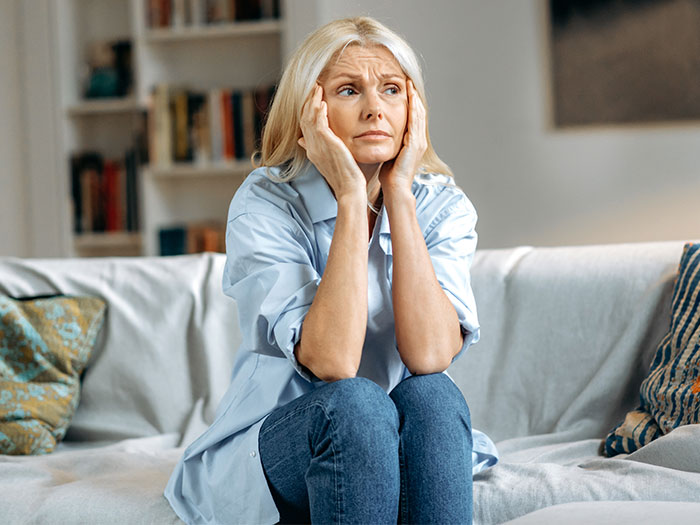Older woman sitting on sofa looking stressed and contemplative, representing MIL tells DIL pregnancy complaints scenario.