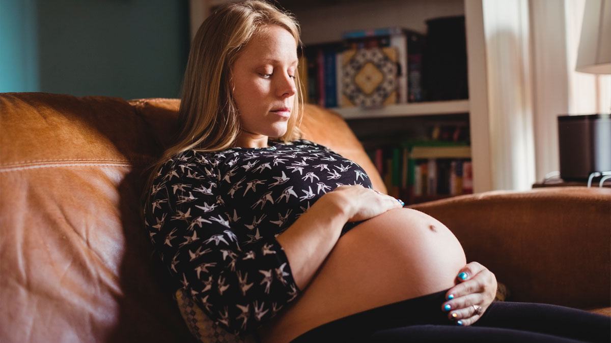 Pregnant woman sitting on a couch with eyes closed, reflecting on MIL telling DIL the world doesn't revolve around pregnancy.