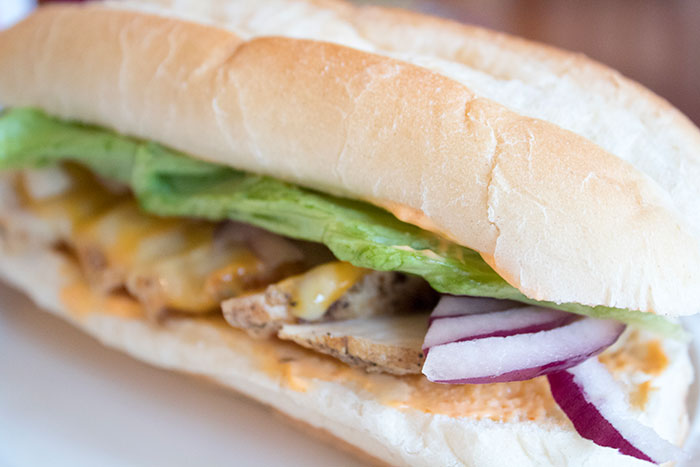 Close-up of a sandwich with grilled chicken, lettuce, onions, and melted cheese illustrating a mildly disturbing fact topic.