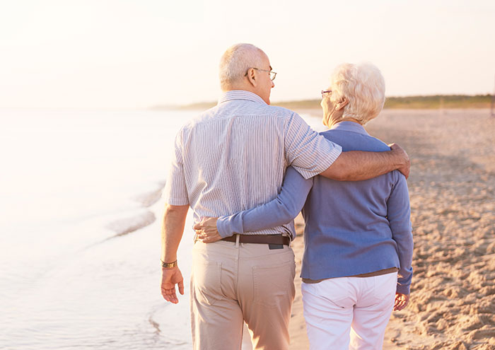Older couple walking on beach at sunset, illustrating a mildly disturbing fact shared by 58 people online.