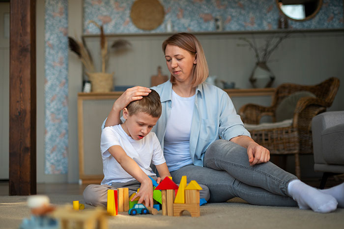 Woman calmly comforting a boy playing with wooden toys indoors, illustrating a mildly disturbing fact concept.