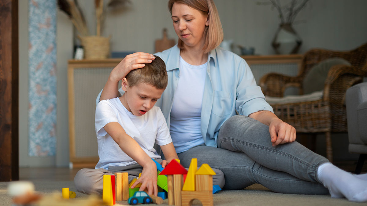 Woman comforting boy playing with wooden blocks indoors showing mildly disturbing fact about child emotions and care