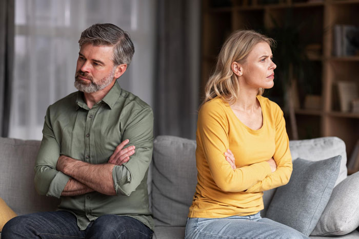 Upset couple sitting apart on couch with crossed arms, showing tension over mom affair and college money issues with dad. Upset couple sitting apart on couch with crossed arms, showing tension over mom affair and college money issues with dad.