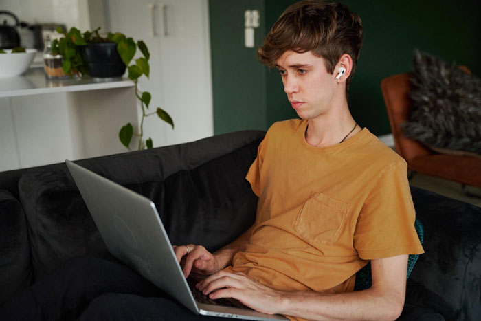 Young man focused on laptop, wearing earbuds, sitting on couch with mom affair college money dad concerns in mind. Young man focused on laptop, wearing earbuds, sitting on couch with mom affair college money dad concerns in mind.