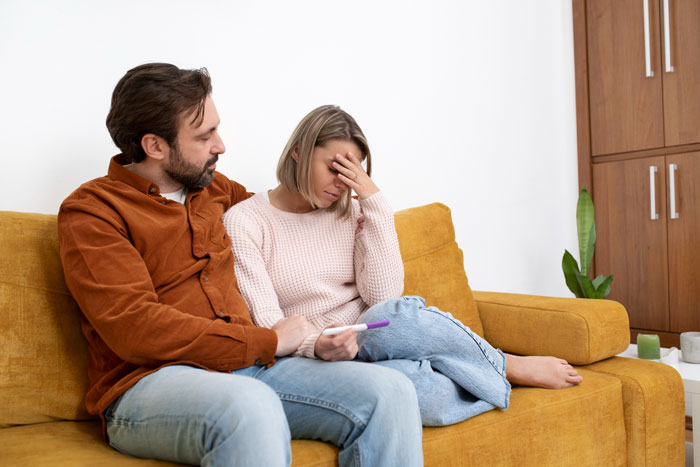 Couple sitting on a couch with the woman upset holding a pregnancy test, capturing a moment of mom affair concern and dad support. Couple sitting on a couch with the woman upset holding a pregnancy test, capturing a moment of mom affair concern and dad support.
