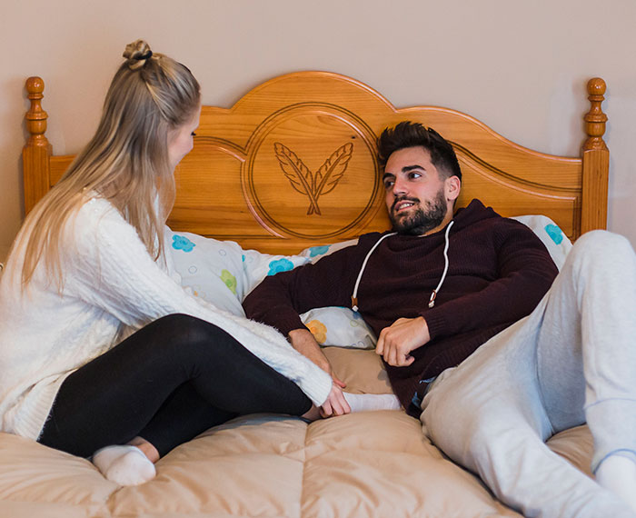 Couple sitting on a bed having a serious conversation, symbolizing man cutting ties with his mother through texts to girlfriend.