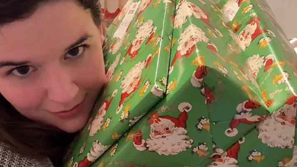 Mom holding large Christmas gifts for her kids, showcasing an insane amount of gifts amid consumerism discussions.