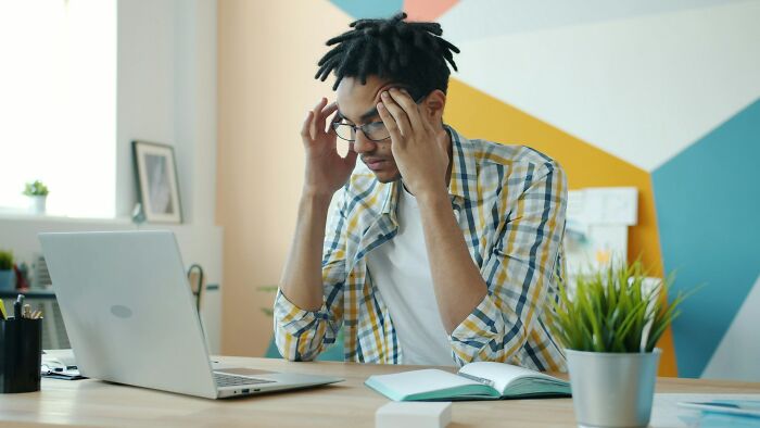 Young man stressed at laptop in colorful office, illustrating inventive ways workers got away with breaking rules.