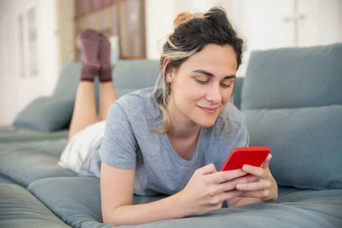 Young woman lying on sofa using smartphone, illustrating hilarious and inventive ways workers got away with breaking rules.