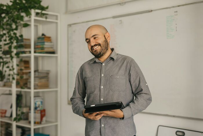 Smiling man holding a tablet in a casual office setting, illustrating hilarious and inventive ways workers broke rules.