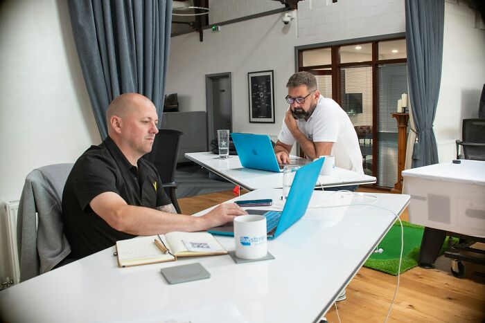 Two workers using laptops at a modern office, showcasing creative ways workers got away with breaking rules.