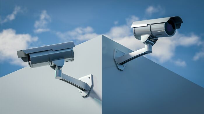 Two security cameras mounted on opposite corners of a building, symbolizing inventive ways workers bypass rules.