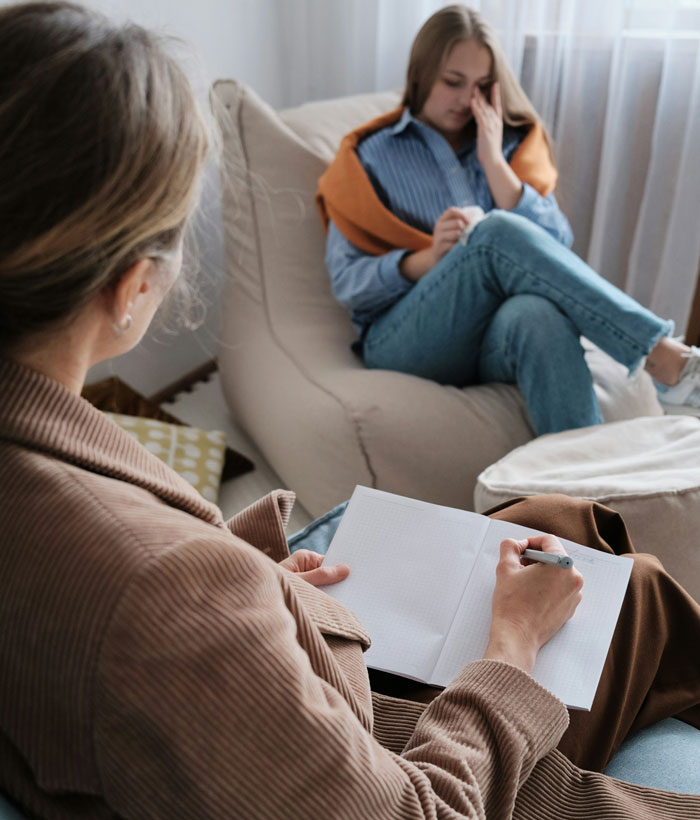 Woman upset during therapy session with counselor taking notes in a cozy, softly lit room setting