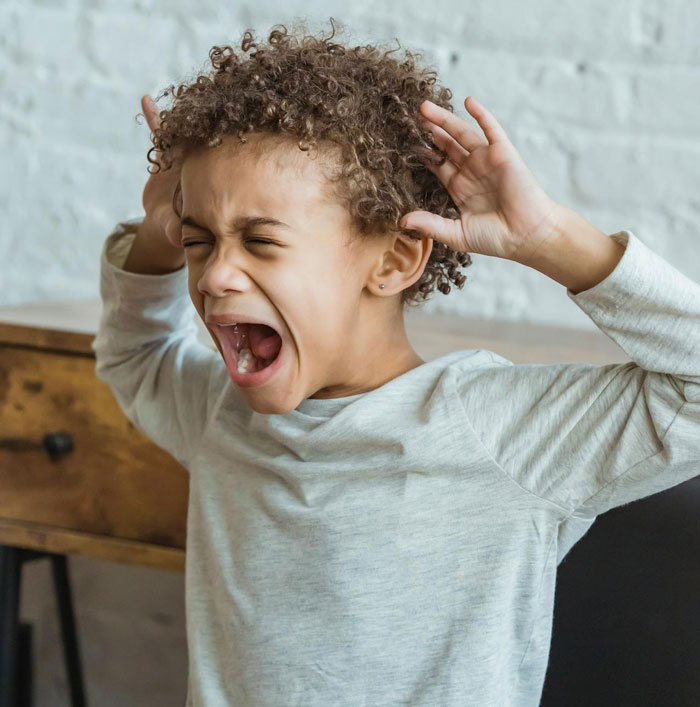 Young child acting out with hands raised and mouth open, illustrating mom's concern about how her kids act behavior.
