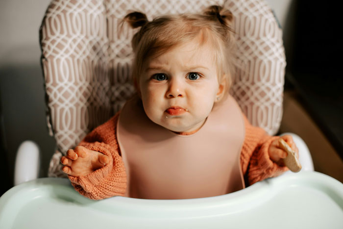 Toddler girl in a high chair looking upset, illustrating mom's concern about how her kids act and behave.