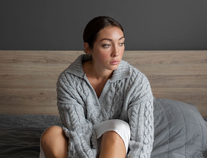 Woman sitting on bed looking upset and distant, reflecting on what SIL thinks about her on Thanksgiving.