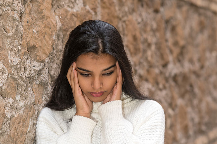 Sad woman in white sweater leaning against stone wall, reflecting on what sister-in-law thinks about her on Thanksgiving.