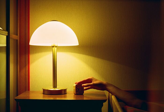 A hand reaching to turn off a bedside lamp, symbolizing subtle signs of cheating in a dimly lit room.