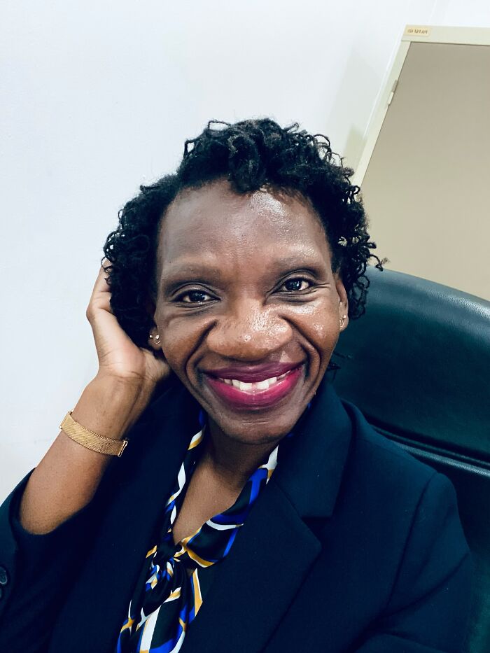 Smiling woman sitting in an office chair wearing a dark blazer and colorful scarf, an internet icon who went viral randomly.