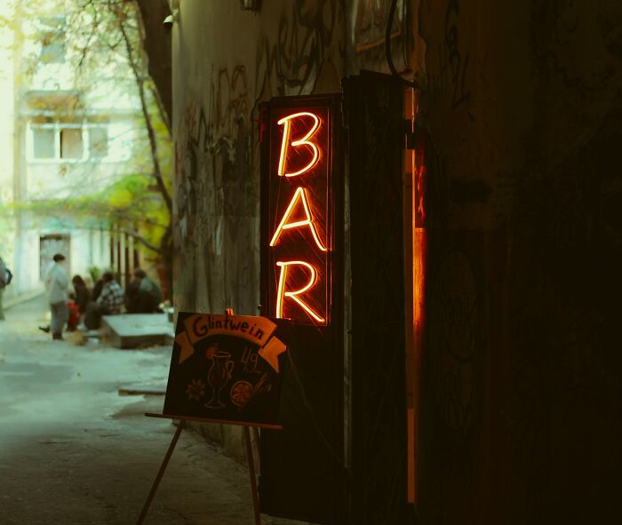 Neon bar sign glowing in a dark alley where people often found out their significant other is unfaithful.