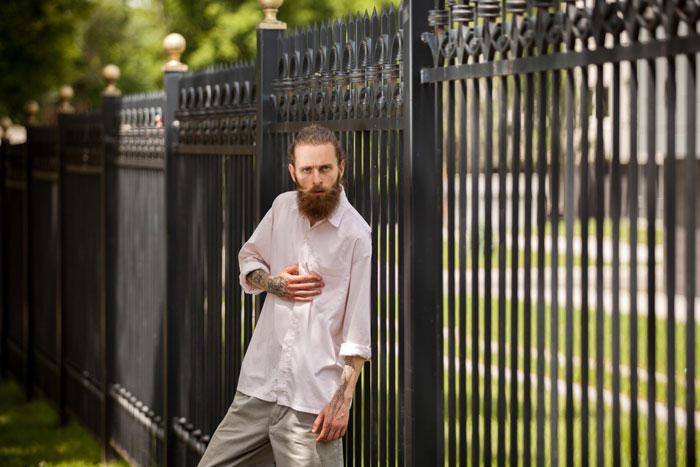 Man with tattoos and beard standing by a new black iron fence after neighbor replaced rotten fence without agreement Man with tattoos and beard standing by a new black iron fence after neighbor replaced rotten fence without agreement