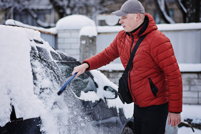 Man in red jacket clearing snow from car window early morning, neighbor comes over to help with panic alarm incident. Man in red jacket clearing snow from car window early morning, neighbor comes over to help with panic alarm incident.