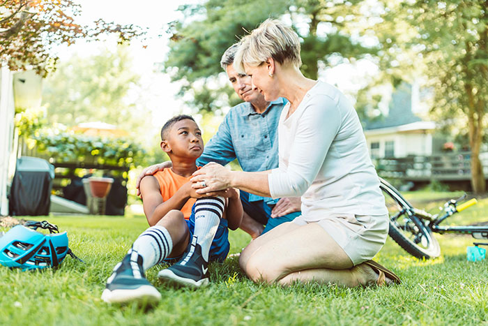 Child sitting on grass with parents caring for injury, highlighting kids using neighbor’s yard without asking. Child sitting on grass with parents caring for injury, highlighting kids using neighbor’s yard without asking.