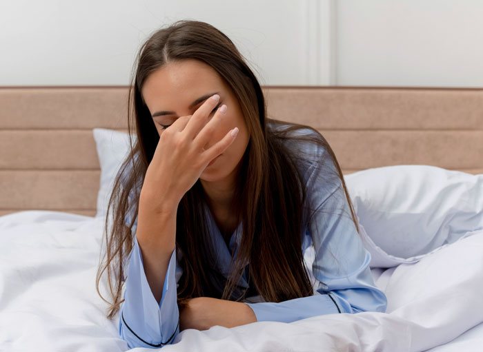 Young woman in blue pajamas on bed covering her face with hand, feeling tired or stressed under actual sun light. Young woman in blue pajamas on bed covering her face with hand, feeling tired or stressed under actual sun light.