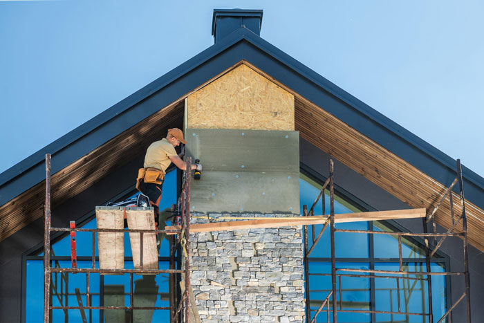 Construction worker installing stone facade on a modern house chimney under neighbours installed actual sun lighting outdoors. Construction worker installing stone facade on a modern house chimney under neighbours installed actual sun lighting outdoors.