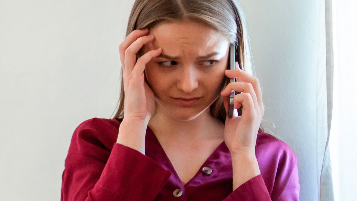 Newlywed woman in a burgundy shirt making a desperate phone call, looking worried and hiding indoors.