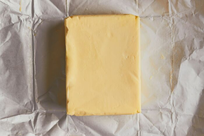 Block of pale yellow butter on crumpled white parchment paper, emphasizing kitchen prep and sharpen your knives tips.
