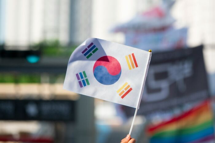 Hand holding South Korean flag outdoors with blurred city background representing smart man from South Korea seeking US asylum Hand holding South Korean flag outdoors with blurred city background representing smart man from South Korea seeking US asylum